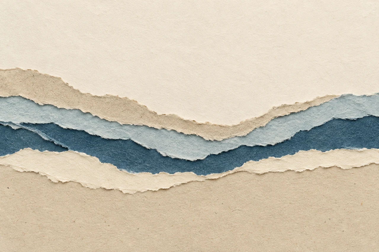 Torn layers of sand, sea-blue and cream paper flow across a wide composition.