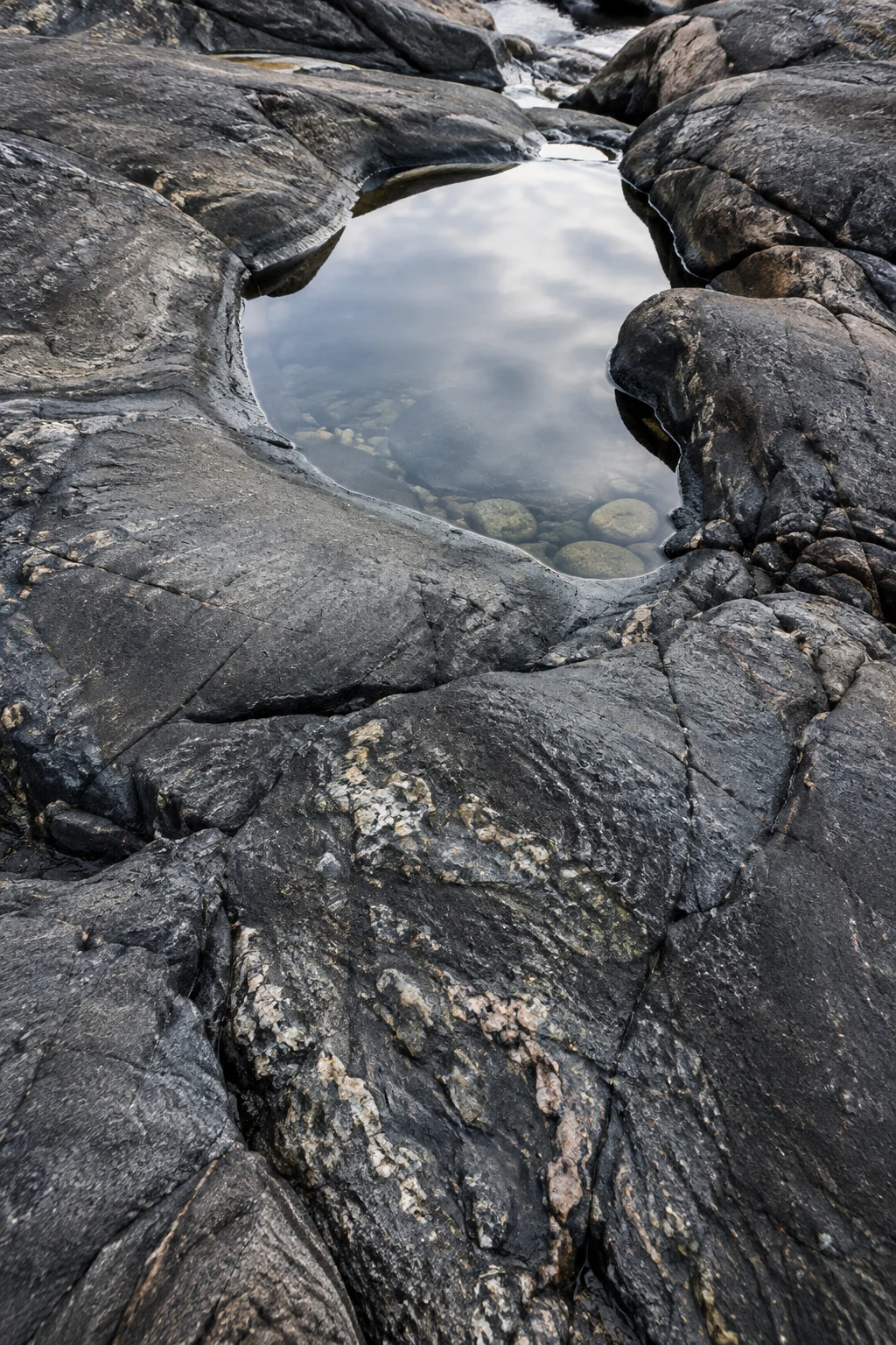 A pale reflection of sky rests in a small tide pool surrounded by dark, weathered stone.